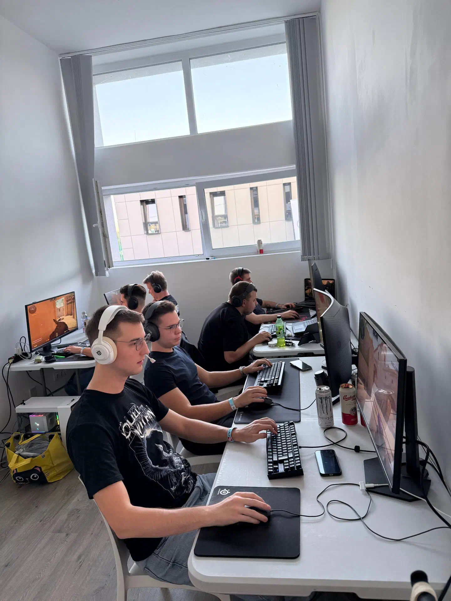 A keskeny teremben fejhallgatós játékosok ülnek egymás mellett a fal menti asztalnál, a monitorokon Counter-Strike 2 fut